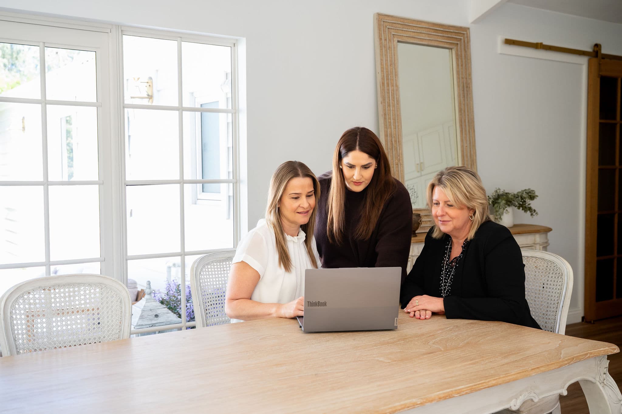 Simone and colleagues reviewing a laptop during a business settlement consultation at a timber table in a bright office.
