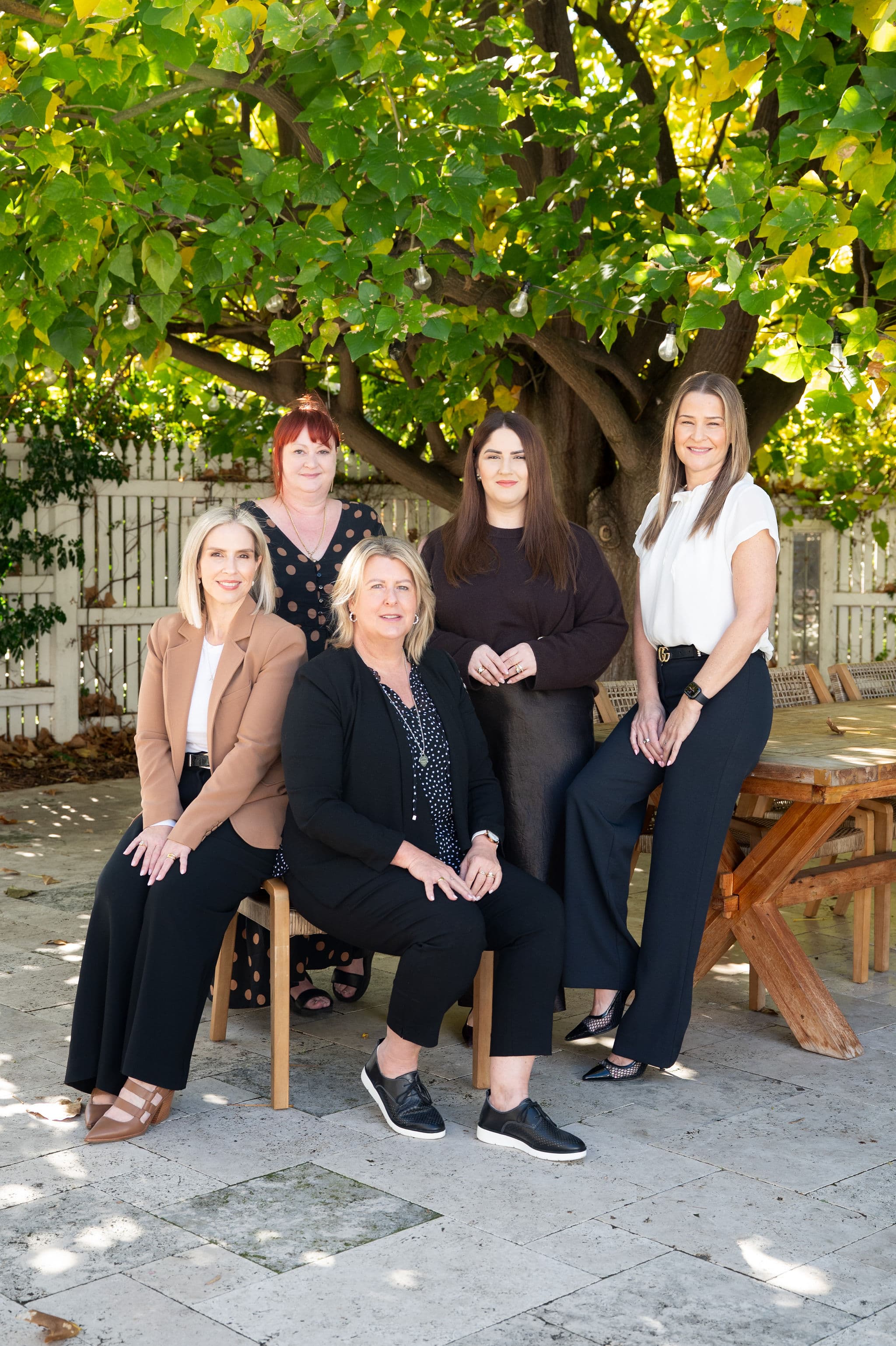 Five team members posing outdoors on a stone patio under a tree with string lights.