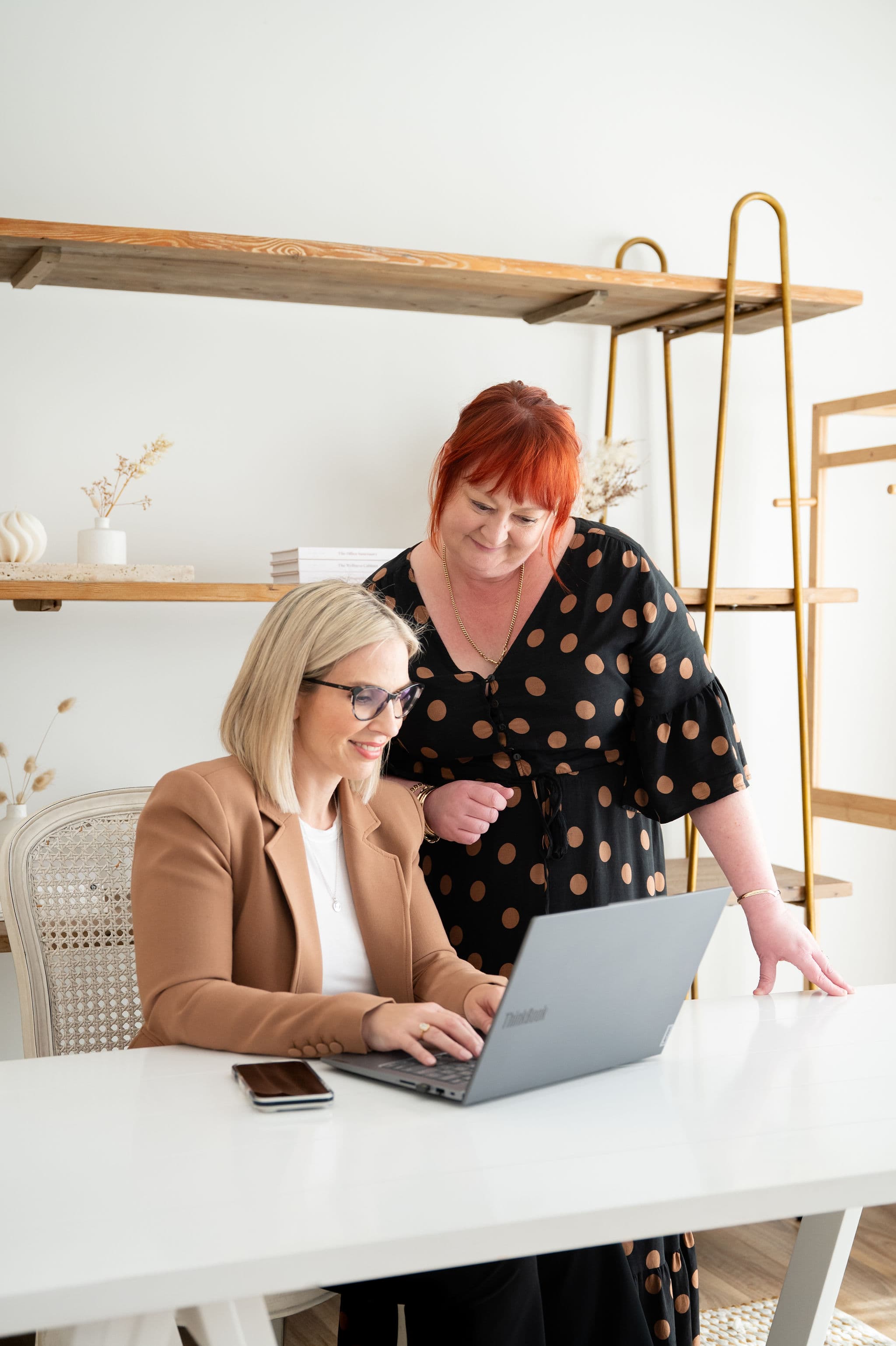 Two team members collaborating over a laptop at a white desk in a modern minimalist office.