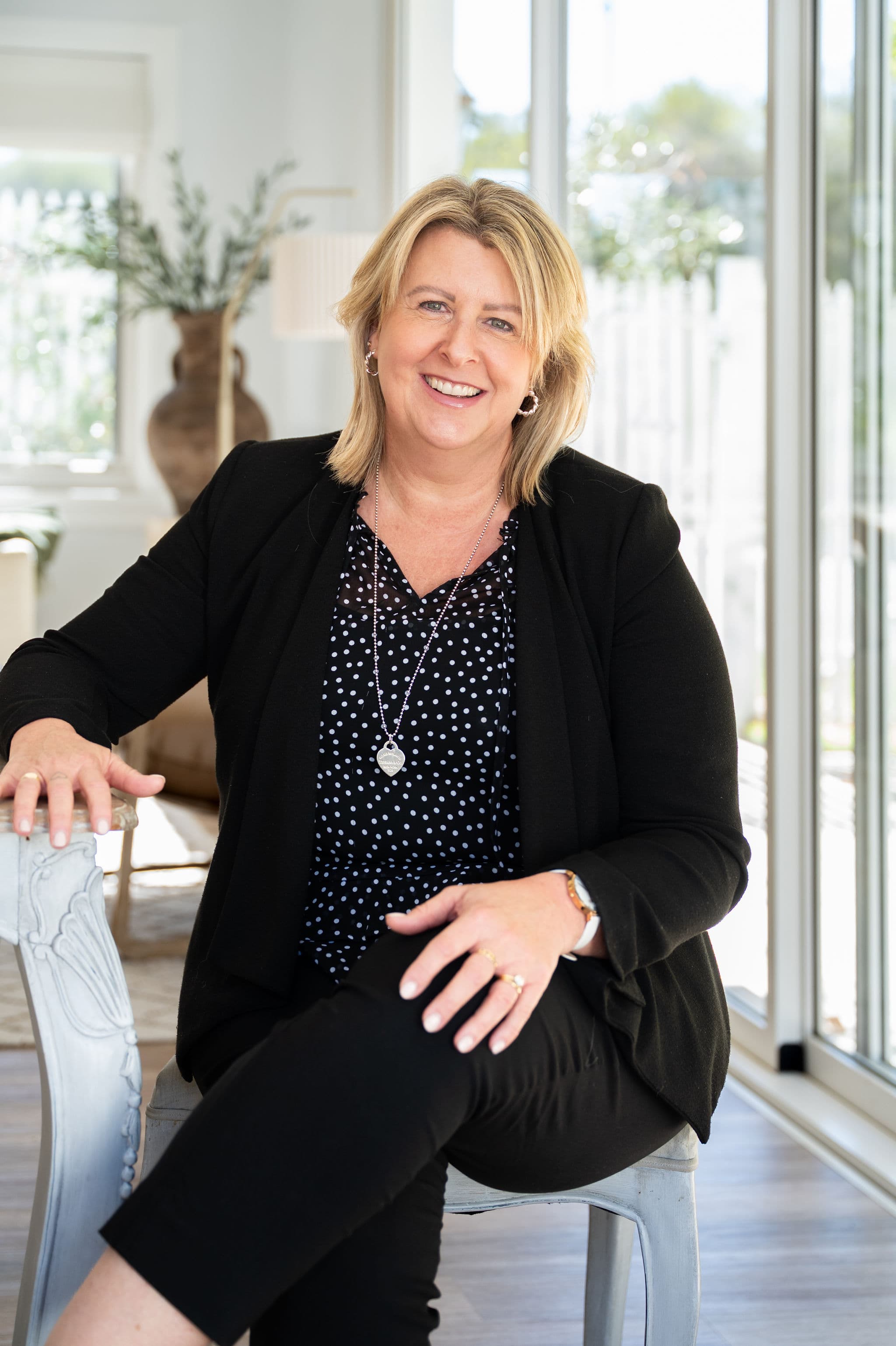 Portrait of Nicky Toomath, conveyancing assistant at West End Settlements, in a black blazer and polka-dot blouse, seated in a bright modern interior.