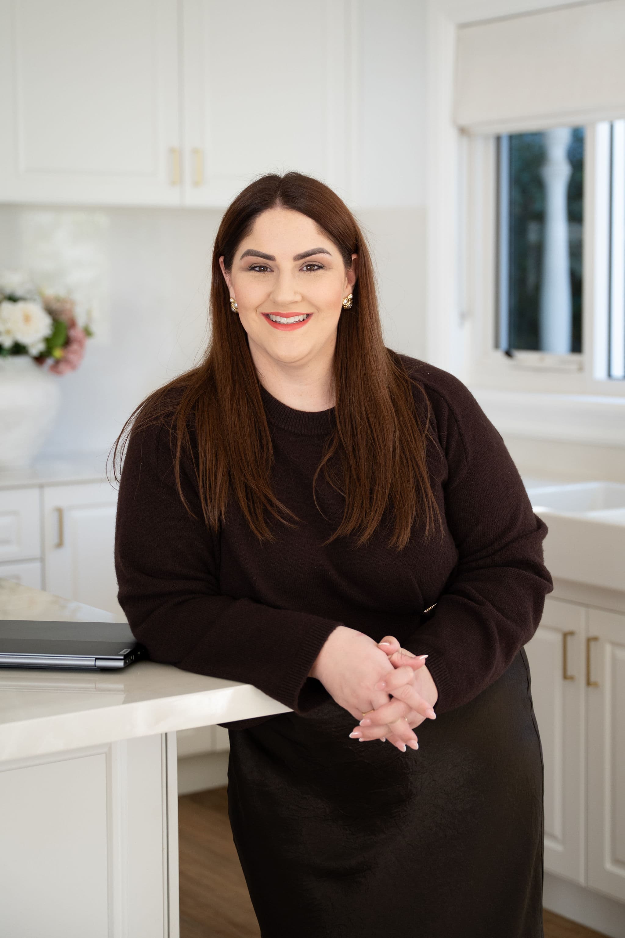 Portrait of a smiling brunette team member leaning on a kitchen counter in a bright modern office.